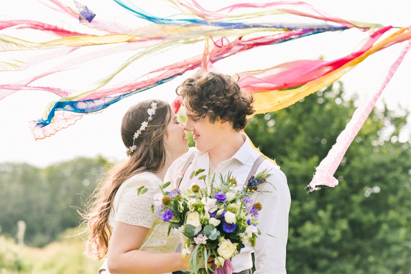 A young couple are about to kiss. There are coloured streamers behind them and she is holding a bouquet of flowers